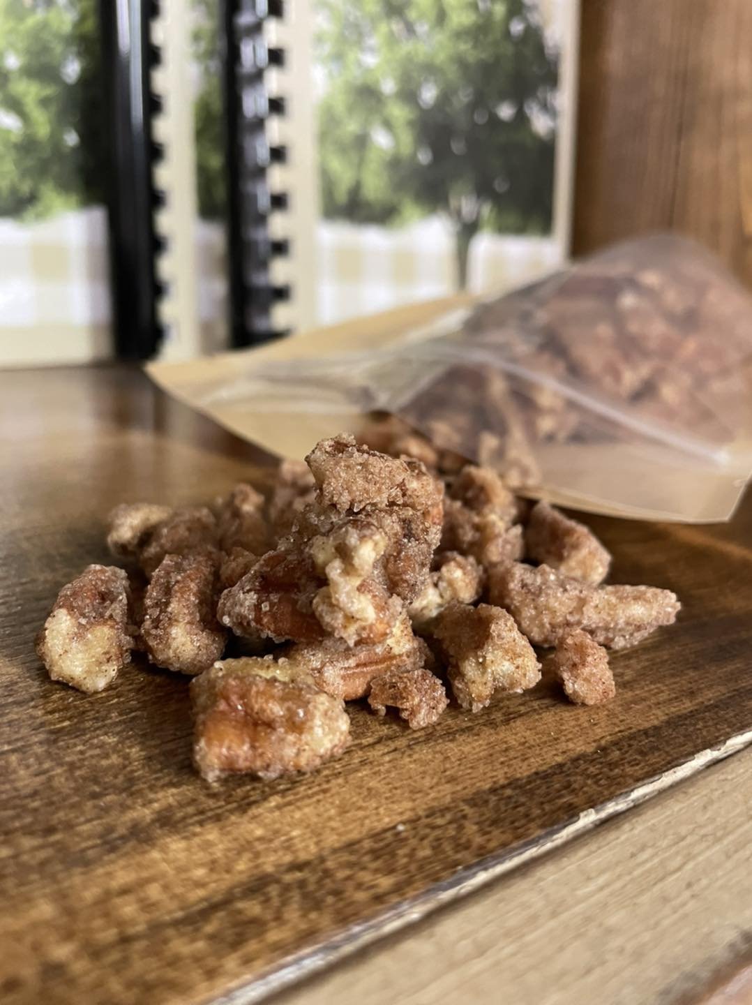 Close-up of sweet, candied pecans scattered on a wooden surface, with a partially open bag of pecans in the background, showcasing a rustic and inviting snack setting.