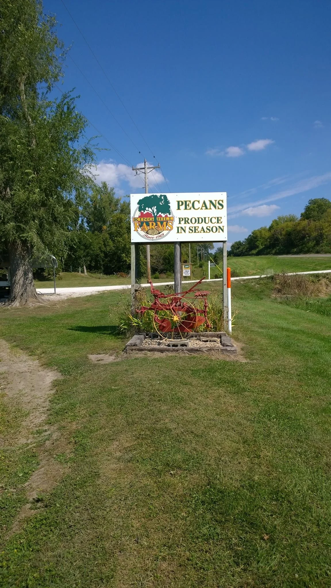 Sign for King Hill Farms advertising seasonal pecans, featuring a decorative red wagon and a clear blue sky in the background.