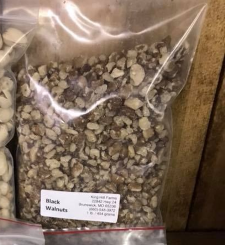 Bag of chopped black walnuts from King Hill Farms, labeled with product details and weight, displayed alongside other nuts on a wooden shelf.