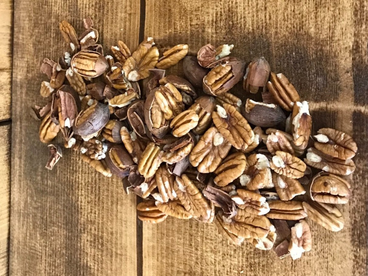 A close-up image of shelled and unshelled pecans scattered on a wooden surface, showcasing their rich brown color and textured shells, ideal for healthy snacking or baking.